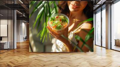 Beautiful girl with a bright salad in her hands on a sunny day smiles and looks at the camera Wall mural