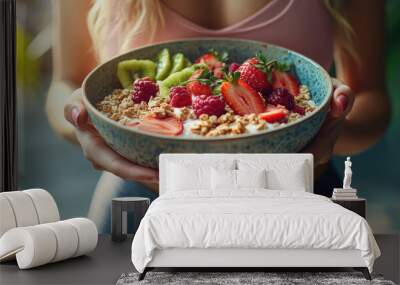 A woman is holding a bowl of fruit and cereal. The bowl is filled with strawberries, kiwi, and granola. The woman is holding the bowl with a smile on her face, indicating that she is happy Wall mural