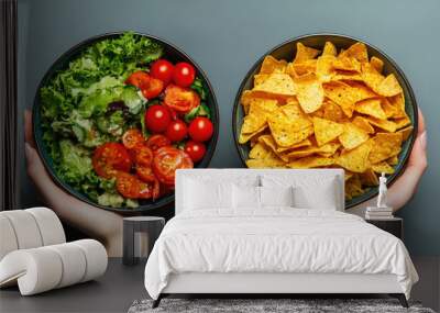 Two bowls of food, one with salad and the other with chips. The person holding the bowls is holding them up to show the difference between the two Wall mural