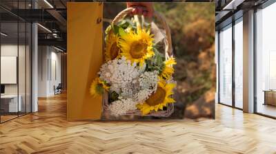 Young woman in yellow dress holding a bouquet of sunflowers to the sunset field. Summer vacation concept, recreation in the countryside, nature beauty, gardening. Wall mural