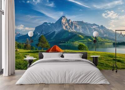 A bright orange tent pitched on a grassy field next to a lake in a beautiful mountain landscape Wall mural