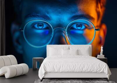 A man with glasses illuminated by a blue light source, creating a striking visual effect on his face Wall mural