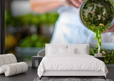 A person is pouring green liquid into a bowl, likely preparing ingredients for a dish using a hand blender Wall mural