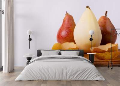 Three pears, one yellow and two red, sit on a wooden cutting board with their peels nearby Wall mural