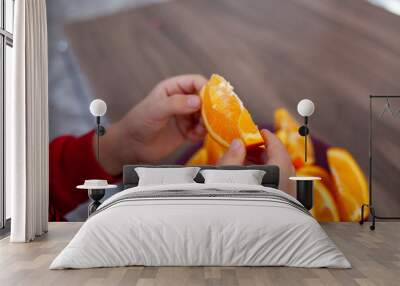 a close-up of a child’s hands holding a slice of orange, with a plate of orange slices on a wooden surface in the background. Wall mural