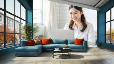 A young Japanese woman with a beautiful smile prepares for a remote work meeting using Zoom etc. while using a computer.Copy space available. Wall mural