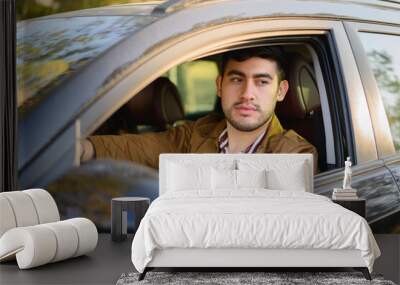 Young stylish Hispanic male driving a modern car under the sunlig Wall mural