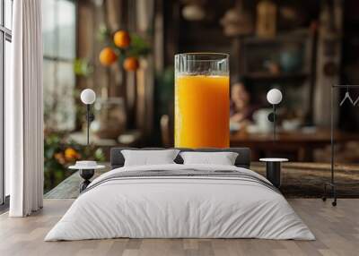 A glass of fresh orange juice sits on the kitchen counter in front, with family having breakfast Wall mural