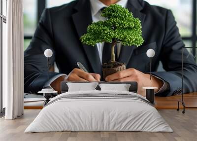 Businessman signing documents with a small tree representing sustainability and growth in a professional setting Wall mural