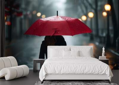 Lonely woman under a vibrant red umbrella amidst a dreary rain-soaked street Wall mural