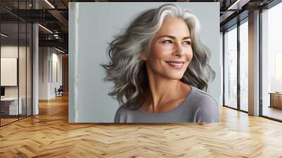 A beautiful smiling senior woman with gray hair and perfect skin in the style of a portrait on a gray background Wall mural