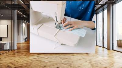 Woman hands using the sewing machine to sew the face home made diy medical mask during the coronavirus pandemia. Wall mural