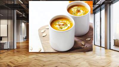 Roasted pumpkin and carrot soup with cream and pumpkin seeds on two white mug on white background with black bread slices.Vegetarian eating.Diet and healthy food concept.Space for copy and text Wall mural