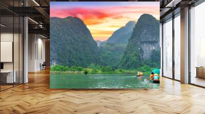 Ninh Binh, Vietnam - April 5th, 2024: Tourists float by boat on the river of the Tam Coc National Park Sightseeing tour to grottoes with sunset sky, Ninh Binh, Vietnam. Wall mural