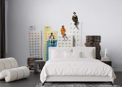 Miniature people sitting on top of a miniature building and pile of coins. Wall mural