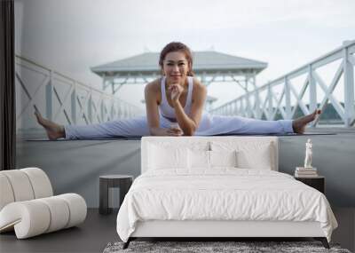 Happy young woman in white clothes practicing yoga. doing splits. stretching in Samakonasana exercise..enjoying sea view, concept for exercising, health care Wall mural