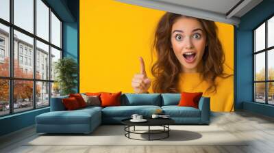 Woman with surprised expression pointing up, yellow background. Wall mural