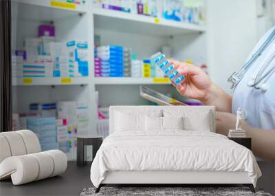 Doctor holding medicine capsule pack and computer tablet for filling prescription in pharmacy drugstore. Wall mural