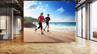 Man and woman running on tropical beach at sunset Wall mural