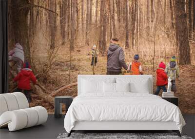 Group of six little kids with a kindergartener running in the forest and climbing trees. Early spring pine forest hike in waldorf kindergarten. Wall mural