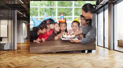 group of happy children girl with hat blowing candles on  birthday cake together celebrating in  party . kids gathered around  birthday cake with nursery teacher in classroom school multiethnic Wall mural