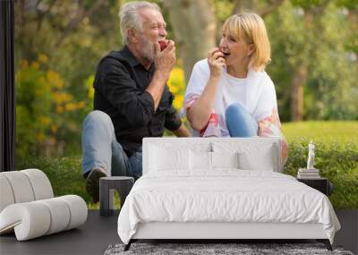 Happy senior couple relaxing in park eating apple together morning time. old people sitting on grass in the autumn park . Elderly resting .mature relationships. family Wall mural