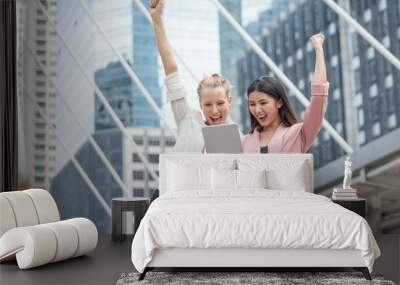 Successful business woman team arms up celebrating with tablet computer in hand in city outdoors . girl excited winner.Cheerful ,happy, female checking online good news . raising hands up Wall mural