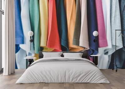 close up collection of colorful t-shirts hanging on clothes hanger in closet or clothing rack Wall mural