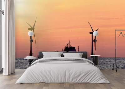 Sustainable resources. Wind farm with ship silhouette at tropical sunrise or sunset. Solar and wind energy and food supply represented. Wall mural