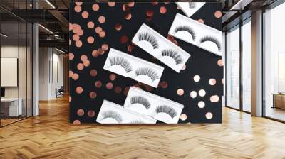 Different fake eyelashes on a festive black background with confetti. Christmas backdrop. Beauty trendy pattern. Makeup accessories. Cosmetics products for women. Closeup. Flat lay.  Wall mural