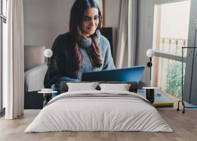 Beautiful smiling young woman sitting at home office working remotely on laptop, Positive female entrepreneur in casual clothes having video chat online at cozy office workplace, E-learning concept Wall mural