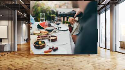 Multi cultural group of people dining together outdoors, Man pouring red wine into glass during cozy family dinner with festive table served with mediterranean food, Friendship Dinner Hanging Out Wall mural