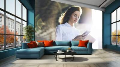 Young smiling businesswoman using modern smartphone outdoors, professional female manager searching information in internet on her mobile phone while working at office, flare light Wall mural