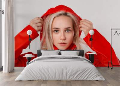 Blond girl gets on hood of a red raincoat isolated over white background. It is starting to rain. Wall mural