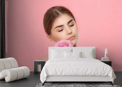 Close-up portrait of a beautiful young girl with pink rose flower isolated over pink background. Wall mural