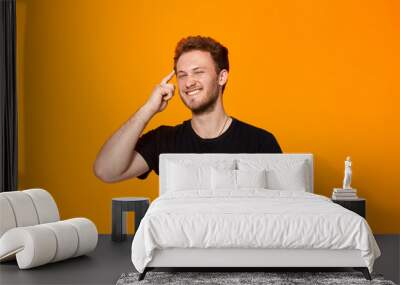 Studio shot of a bearded young man pointing a finger at the temple. Concept of a positive thinking. Wall mural