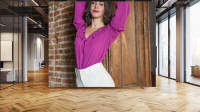 Beautiful young brunette woman in a purple blouse and white pants posing outdoor. Portrait of a beautiful young brunette woman with long hair posing fashion Wall mural