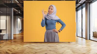 happy asian indonesian muslim woman giving ok finger gesture on isolated yellow background Wall mural