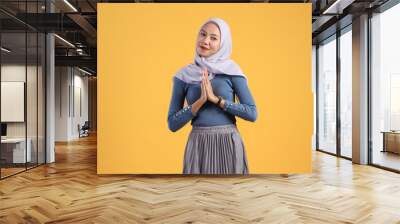 Happy asian indonesian muslim woman wearing hijab with greeting hand on isolated yellow background Wall mural