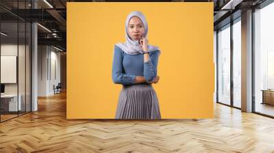 pensive asian indonesian muslim woman with thinking gesture on isolated yellow background Wall mural