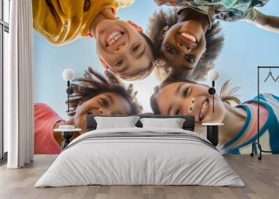 A group of happy, diverse children huddled in a circle, looking down and smiling at the camera, representing unity, friendship, and multicultural togetherness Wall mural