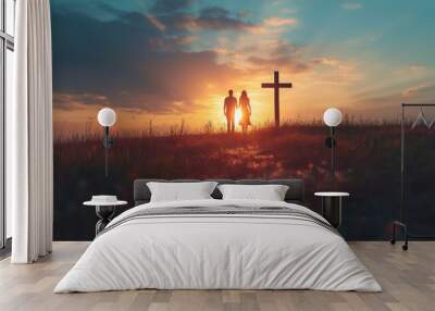 Couple praying together in field in front of cross at sunset Wall mural