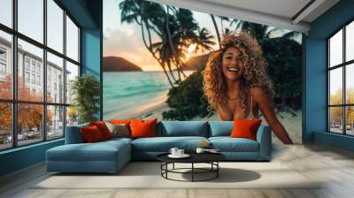 young woman with curly hair in a bikini enjoys a tropical beach at sunset, smiling joyfully with the ocean and palm trees in the background Wall mural