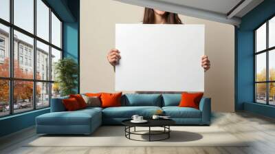 Woman Holding a Blank White Poster in Front of a Beige Wall Wall mural