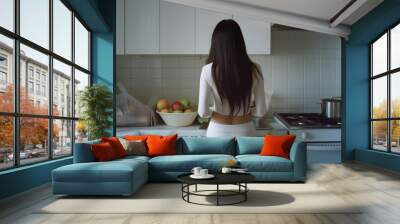 A woman in white workout attire is preparing a meal in the kitchen. Wall mural