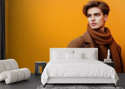 A young man poses confidently in a stylish sweater and scarf, set against a orange background Wall mural