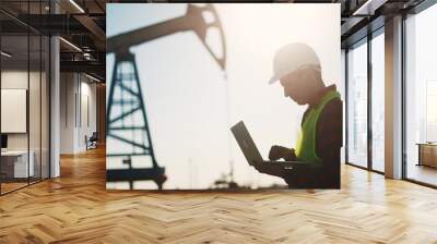 oil business. a worker works next to an oil pump holding a laptop. industry business oil and gas concept. lifestyle engineer studying the level of oil production on a laptop silhouette at sunset Wall mural