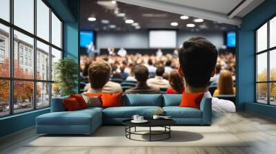 Business symposium speaker on stage with audience sitting in lecture hall viewed from behind Wall mural