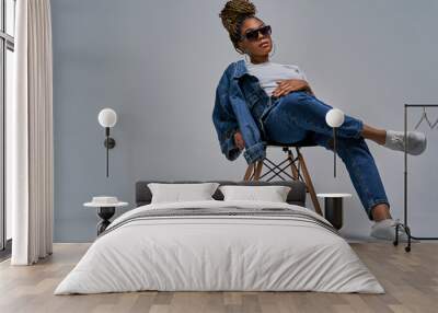 Relaxing girl in sunglasses in white t-shirt in jeans  in sneakers posing on camera sitting on chair with leg lies on the knee. Fashion concept Wall mural