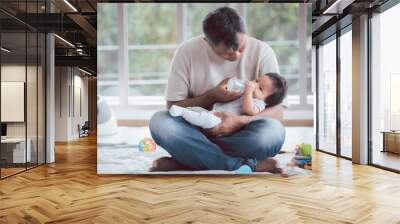 Asian father holding and feeding her baby boy with milk from baby bottle. Wall mural